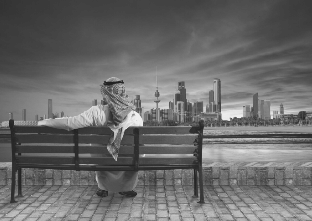 Homem sentado num banco a olhar para a cidade do Kuwait