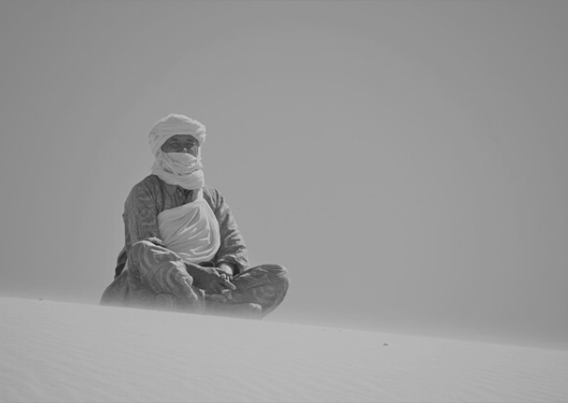 Homem sentado numa duna no deserto na Argélia